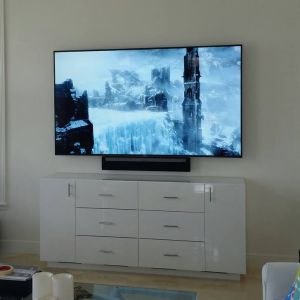 A television wall-mounted above a white gloss sideboard, with a slim soundbar fixed directly beneath the screen.