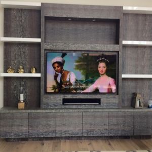 A grey oak media wall with open shelving and gold ornaments, built around a large television and soundbar.