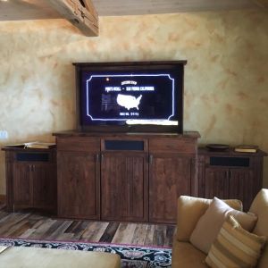 A television set into a dark wood cabinet against a textured plaster wall, in a room with exposed ceiling beams.