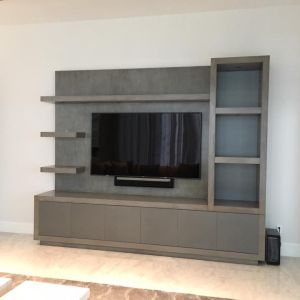 A grey media wall unit with floating shelves and a frosted-glass display cabinet, built around a wall-mounted television and soundbar.