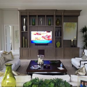 A grey-brown wooden entertainment unit with glass display shelves and a television, in a formal living room.