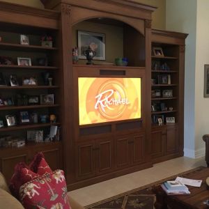 A traditional wooden entertainment unit with an arched surround housing a television, flanked by bookshelves of framed photographs.